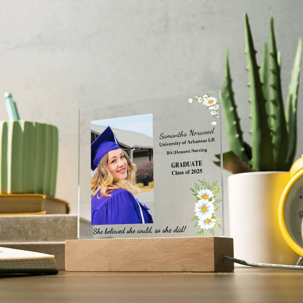 "Personalized acrylic graduation plaque with the graduate's name, school, degree, and the quote 'She believed she could, and she did,' displayed on a wooden LED base with 7 color-changing options."