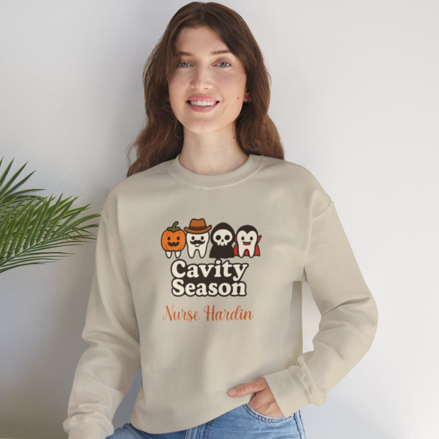 Woman wearing a beige Halloween-themed sweatshirt that says "Cavity Season" with four cute tooth characters in costumes (pumpkin, cowboy, skull, and vampire) and personalized with the name "Nurse Hardin."