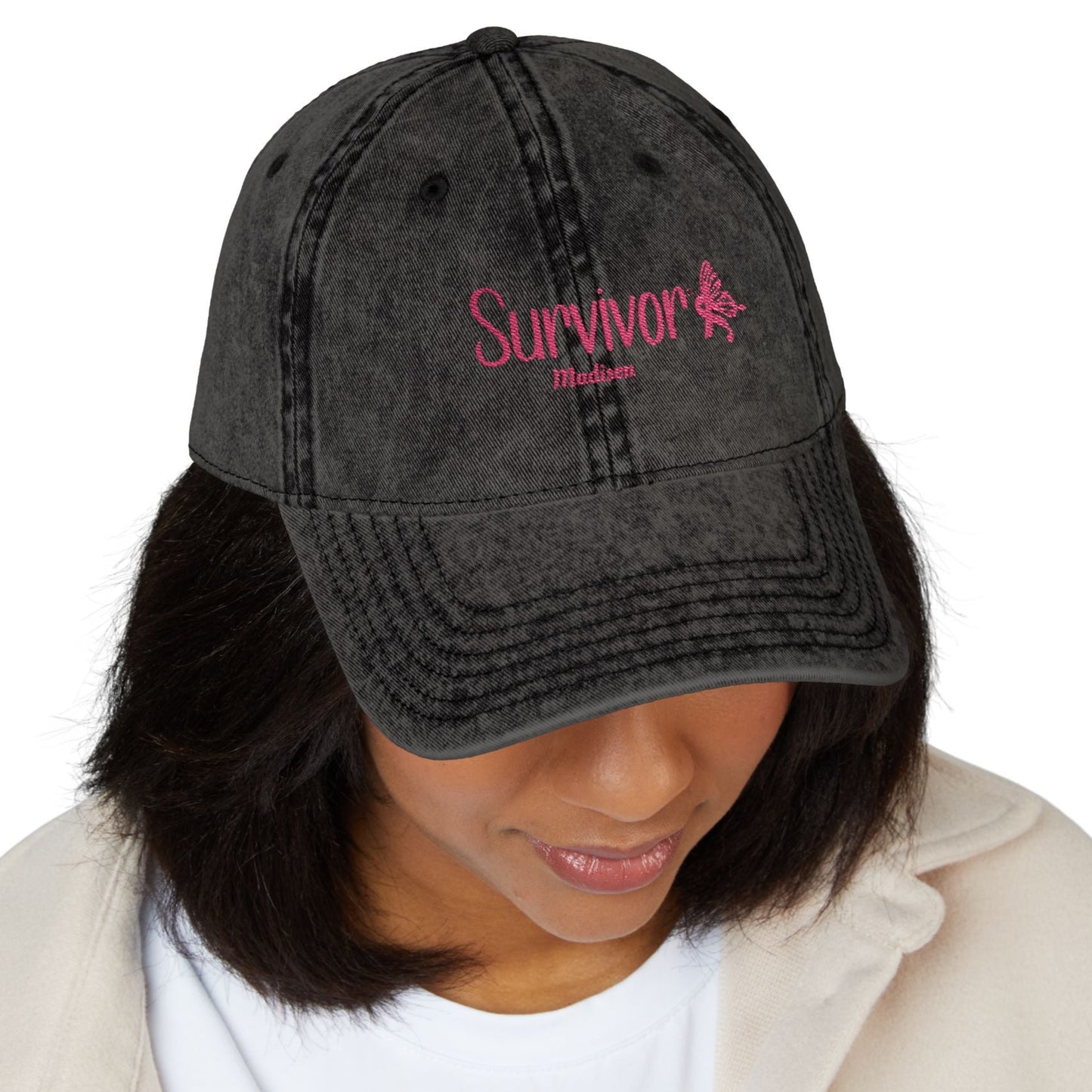 “Vintage Survivor embroidered cap in black washed cotton twill with pink embroidery, distressed finish, and adjustable antique brass buckle.”