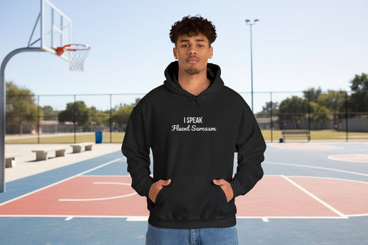 Man wearing black embroidered pullover hoodie with "I Speak Fluent Sarcasm" text in white on chest, standing on outdoor basketball court with kangaroo pocket and hood