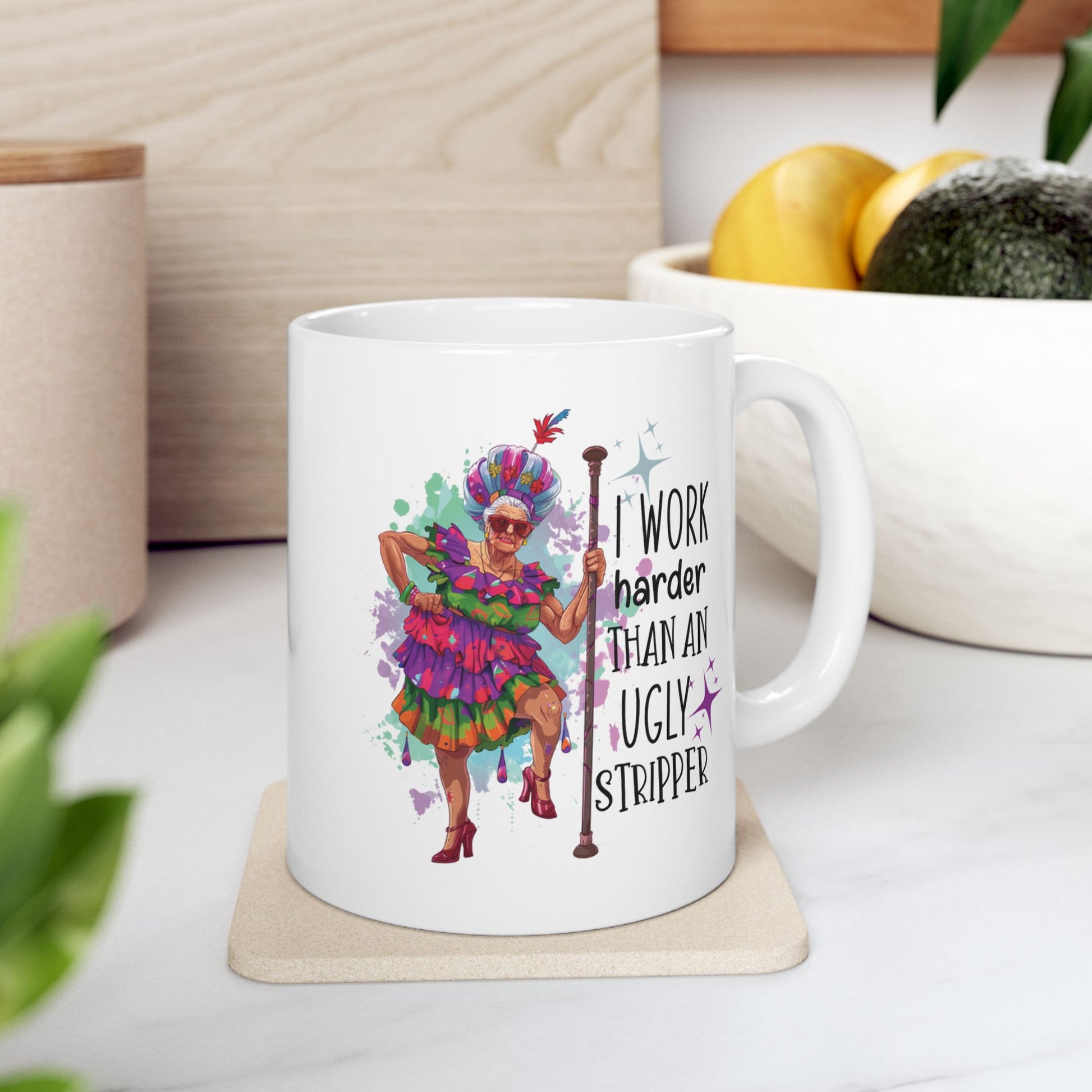 White ceramic mug on kitchen counter featuring a colorful, flamboyant elderly woman with a cane and the phrase “I Work Harder Than an Ugly Stripper” in bold, playful font
