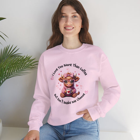 Light pink crewneck sweatshirt featuring adorable illustrated cow wearing glasses and holding a coffee mug, surrounded by hearts, with text "I love you more than coffee but don't make me choose"