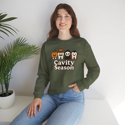 Woman wearing a dark green "Cavity Season" Halloween sweatshirt with four cartoon teeth dressed in festive costumes – pumpkin, cowboy, skeleton, and vampire – perfect for fall and spooky season celebrations.
