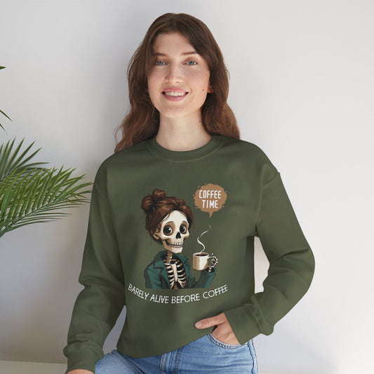 "Smiling woman wearing an olive green sweatshirt with a skeleton holding coffee and text that reads 'Barely Alive Before Coffee – Coffee Time' – funny coffee lover crewneck"