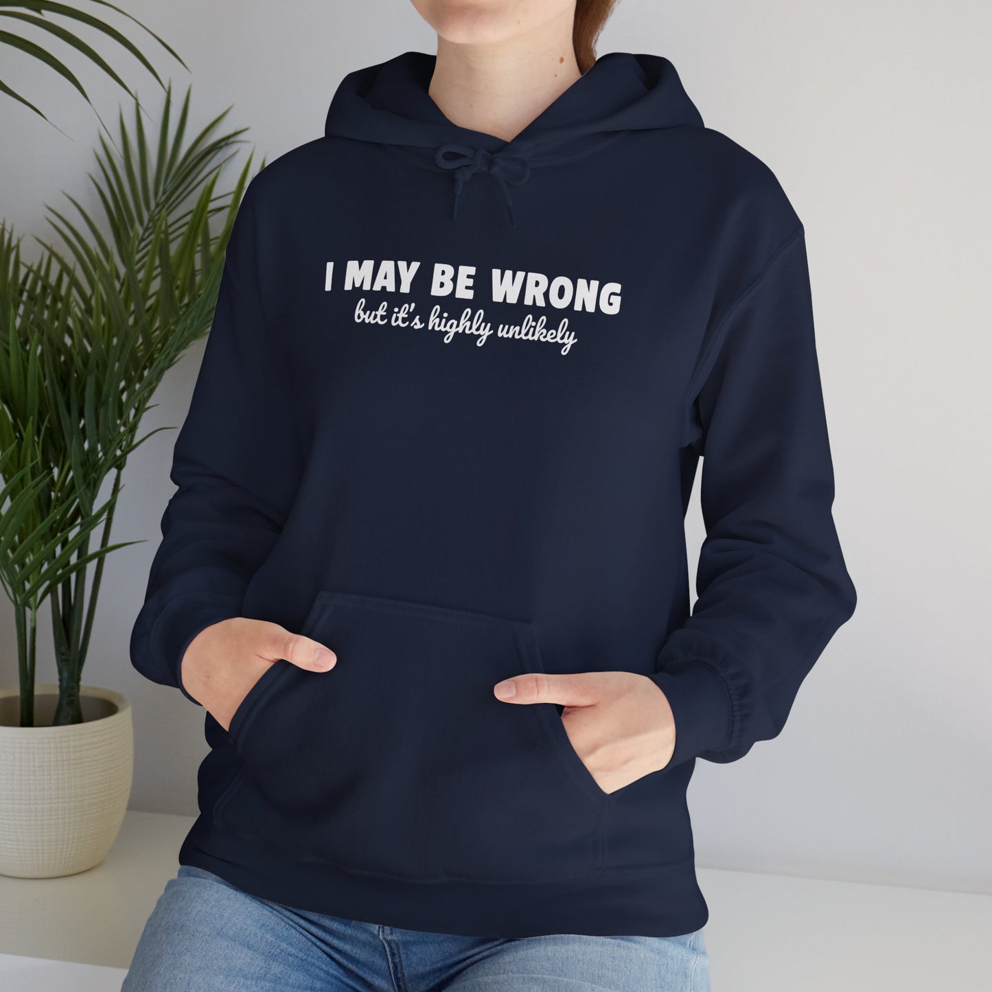 Woman wearing navy blue pullover hoodie with "I May Be Wrong But It's Highly Unlikely" white text print, kangaroo pocket, cozy cotton poly blend, funny sarcastic statement sweatshirt, casual home wear