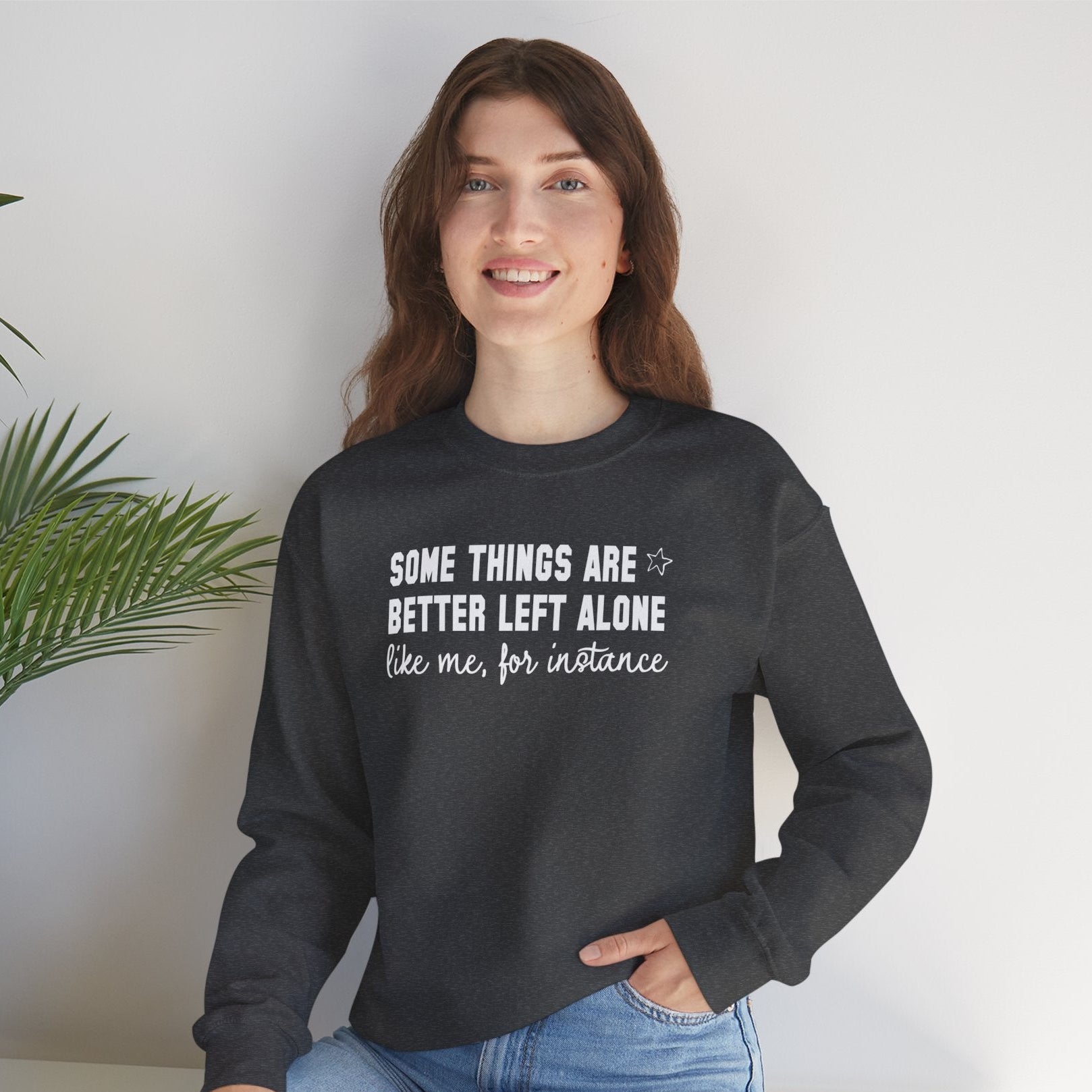 Woman wearing black crewneck sweatshirt with white sarcastic quote “Some Things Are Better Left Alone Like Me For Instance” in minimalist graphic design.