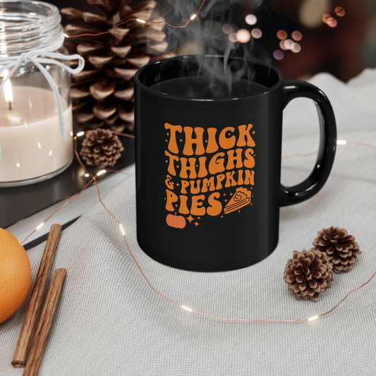  Black ceramic coffee mug with orange text reading "Thick Thighs &amp; Pumpkin Pies" surrounded by fall decorations including pinecones, cinnamon sticks, and warm lighting, perfect for Halloween and Thanksgiving celebrations
