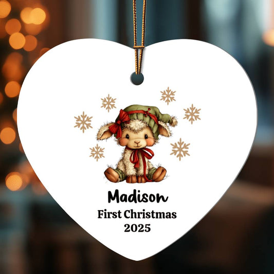 Personalized white heart-shaped Christmas ornament featuring adorable lamb wearing green hat and red bow, surrounded by gold snowflakes, with customizable name "Madison" and text "First Christmas 2025" printed below