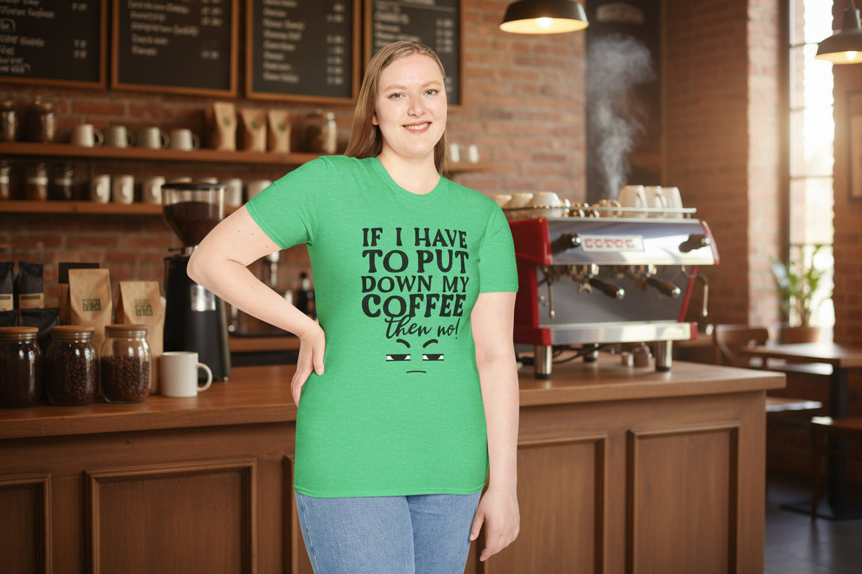 Woman smiling and wearing a green heather unisex t-shirt inside a coffee shop, featuring a bold black hand-lettered graphic that reads "If I Have to Put Down My Coffee, Then No" with a grumpy side-eye face illustration