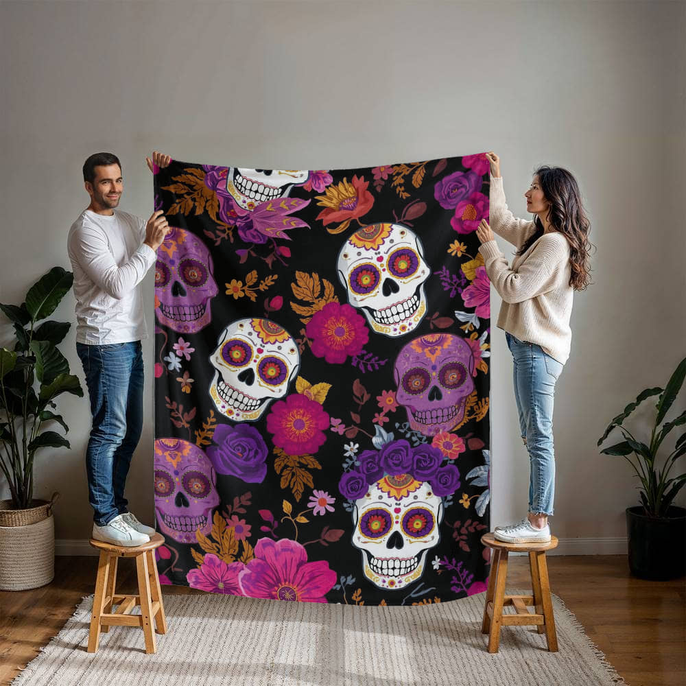 Couple holding a large Mink Touch Fleece Blanket featuring colorful Día de los Muertos sugar skulls and floral patterns in magenta, purple, and gold on a black background.