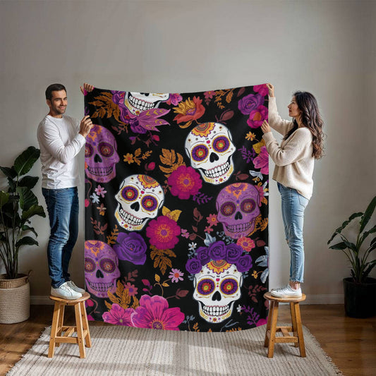 Couple holding a large Mink Touch Fleece Blanket featuring colorful Día de los Muertos sugar skulls and floral patterns in magenta, purple, and gold on a black background.