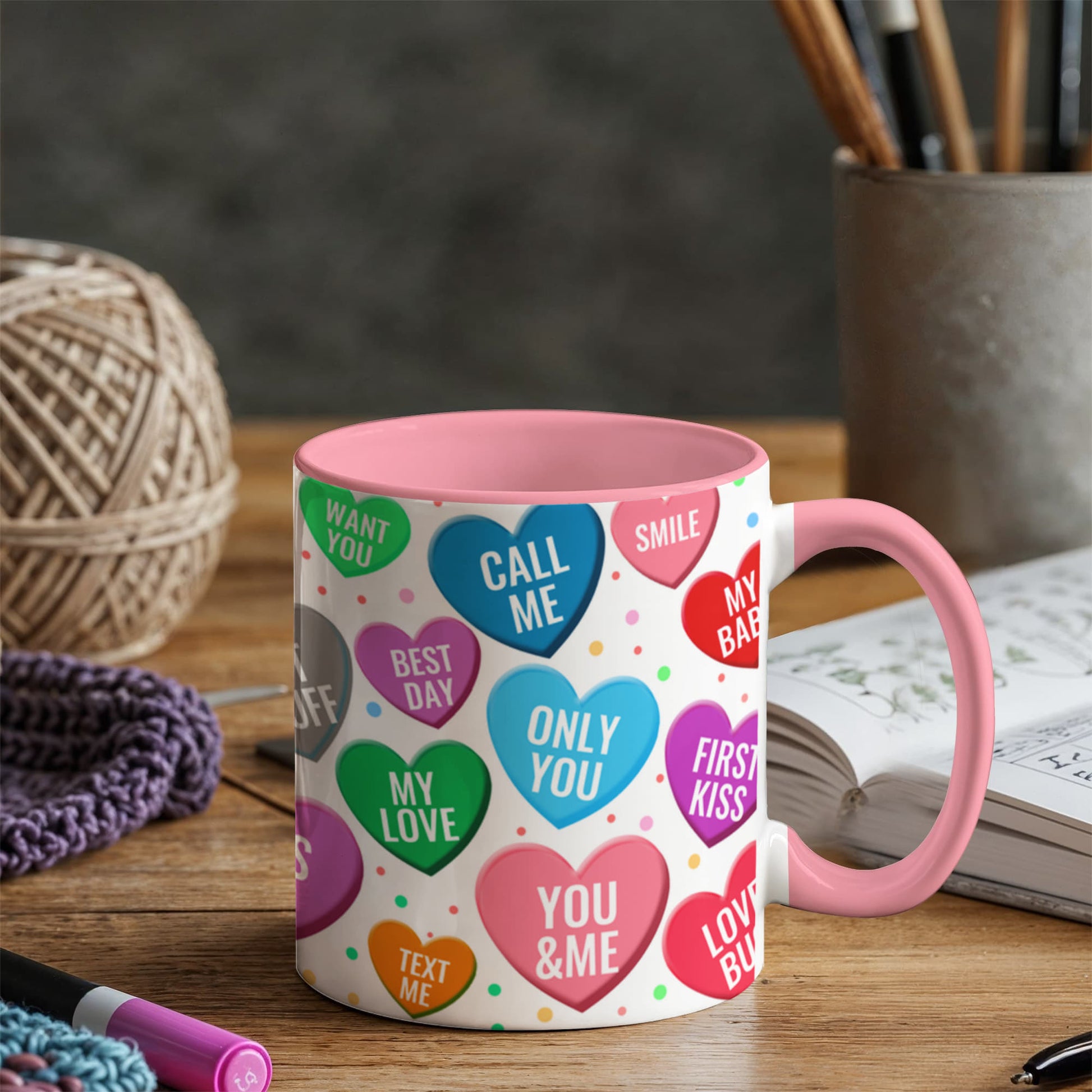 Pink and white ceramic coffee mug with colorful conversation heart candies pattern featuring romantic messages like Call Me, Only You, My Love, Best Day, and Text Me, displayed on wooden table