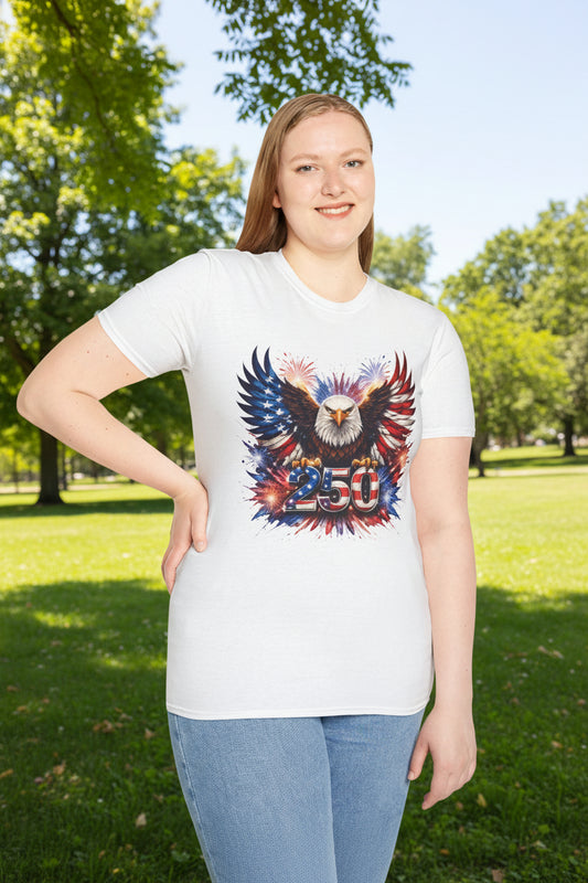 Woman wearing a white patriotic graphic t-shirt featuring a bald eagle with American flag wings, fireworks, and “250” Americana artwork outdoors in a park.