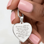 Close-up of engraved stainless steel heart necklace held by hand, featuring sentimental message and adjustable snake chain, personalized jewelry gift.