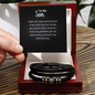 Black multi-strand braided leather men's bracelet with stainless steel cross beads and "love you forever" engraving displayed in mahogany gift box with "To My Son" inspirational message card held by hand