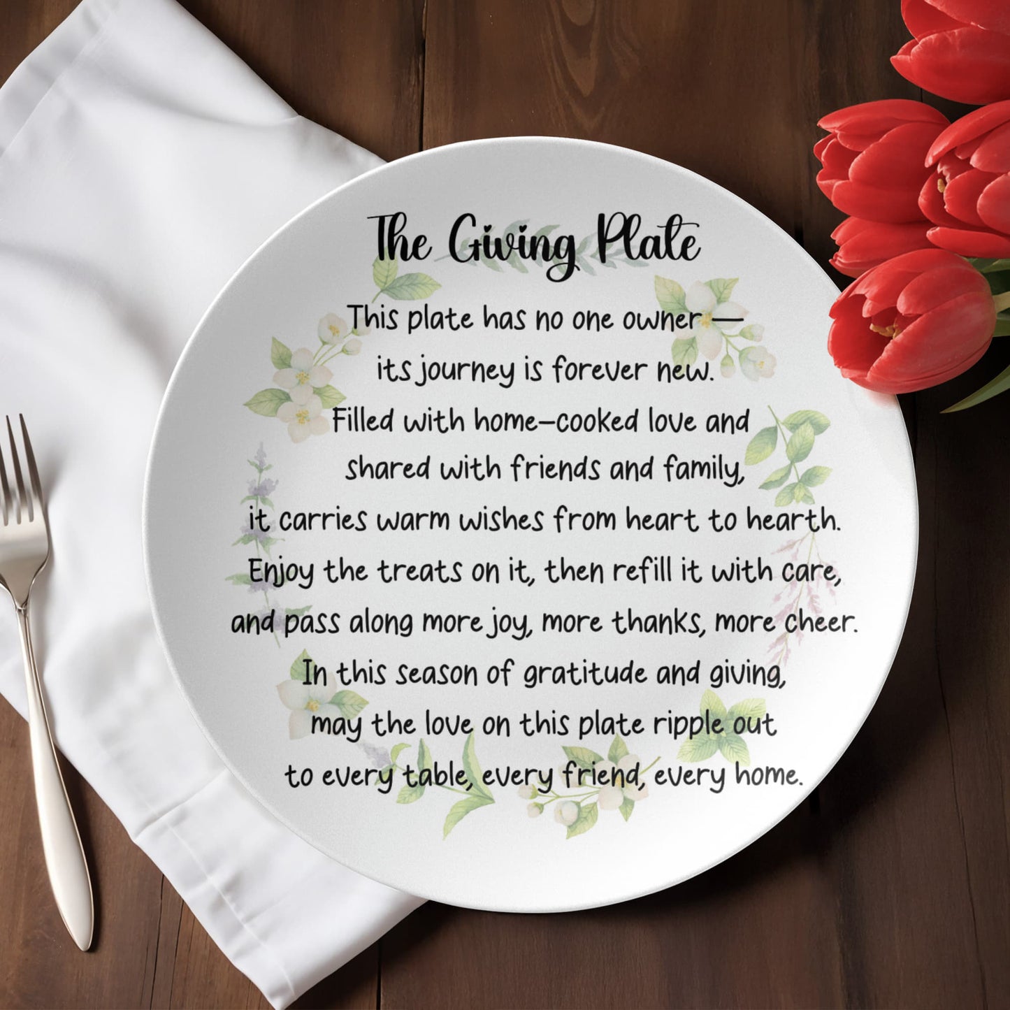 The Giving Plate - white 10 inch ceramic dinner plate with black inspirational text and green floral watercolor design about sharing love and gratitude, displayed on white napkin with fork and red tulips
