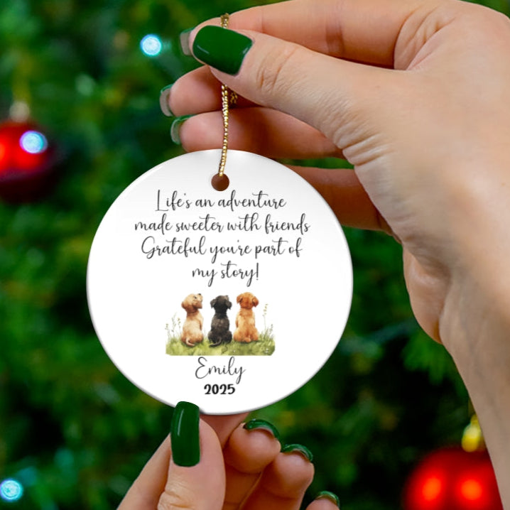 Hand holding a personalized ornament with text and images of dogs against a Christmas tree background.