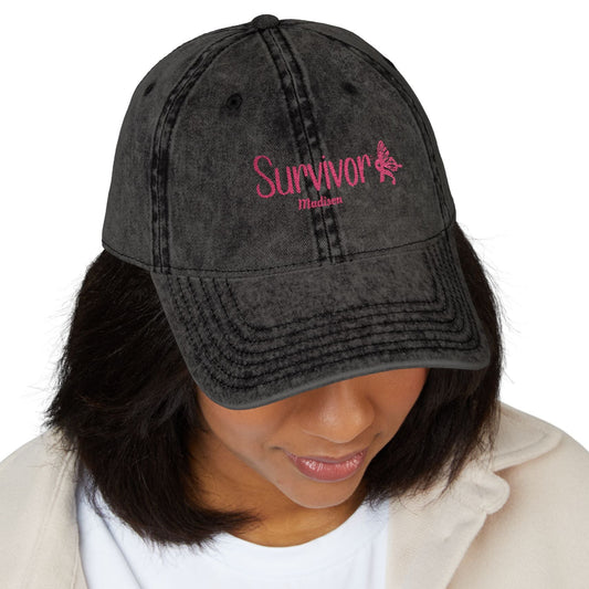 “Vintage Survivor embroidered cap in black washed cotton twill with pink embroidery, distressed finish, and adjustable antique brass buckle.”